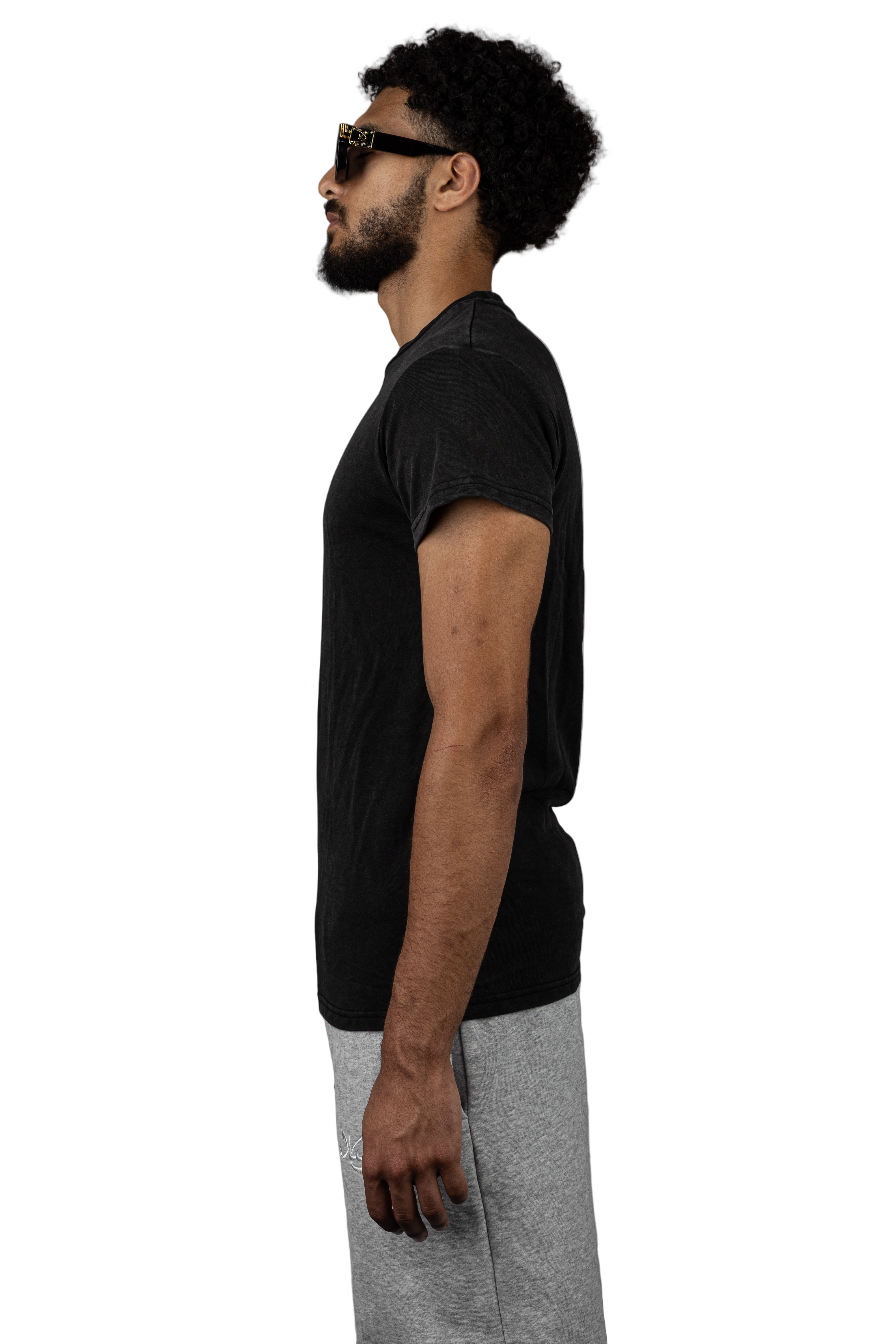 Man wearing a Salaam black t-shirt and gray pants against a gray background