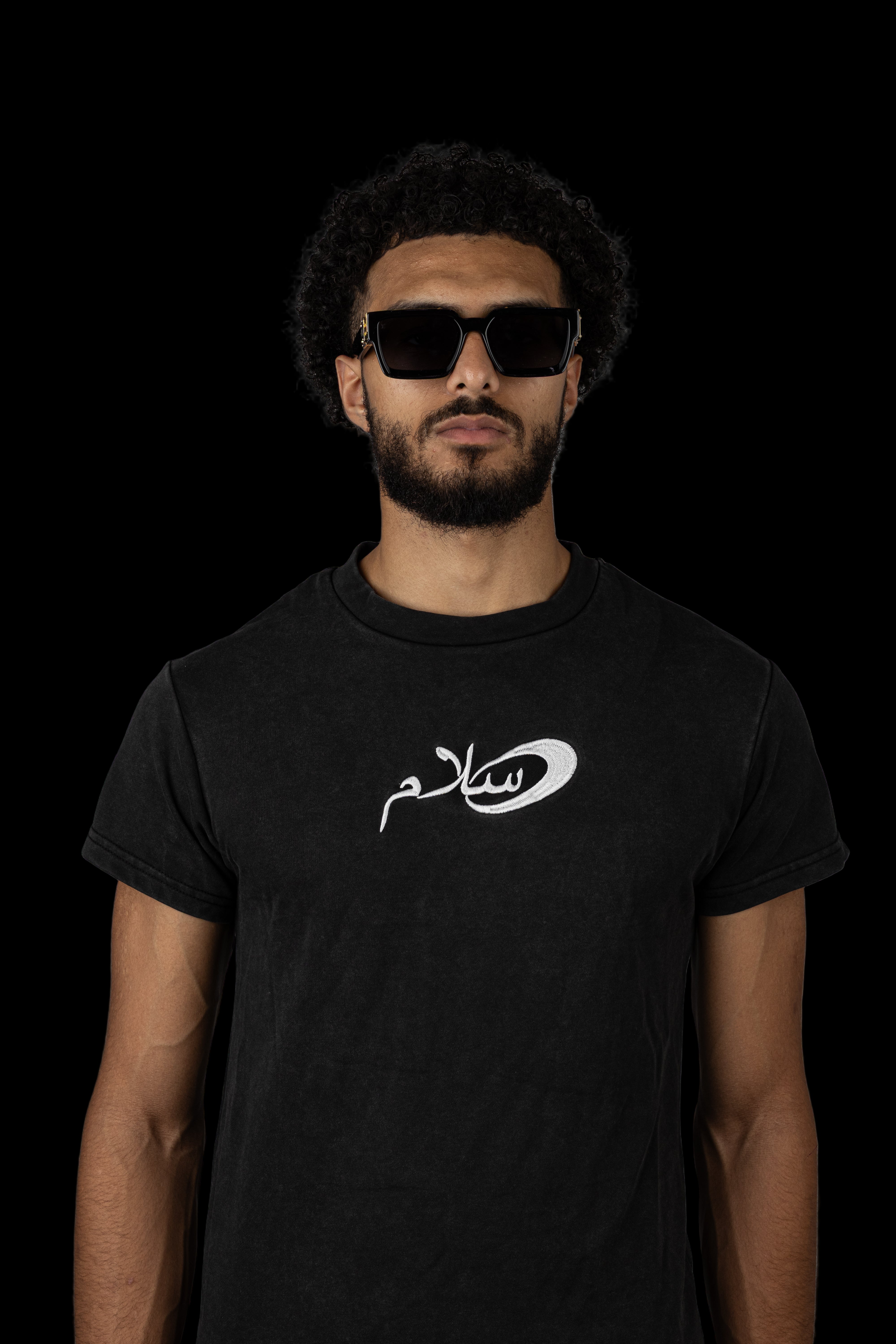Man wearing a salaam black t-shirt with  salaam logo against a gray background